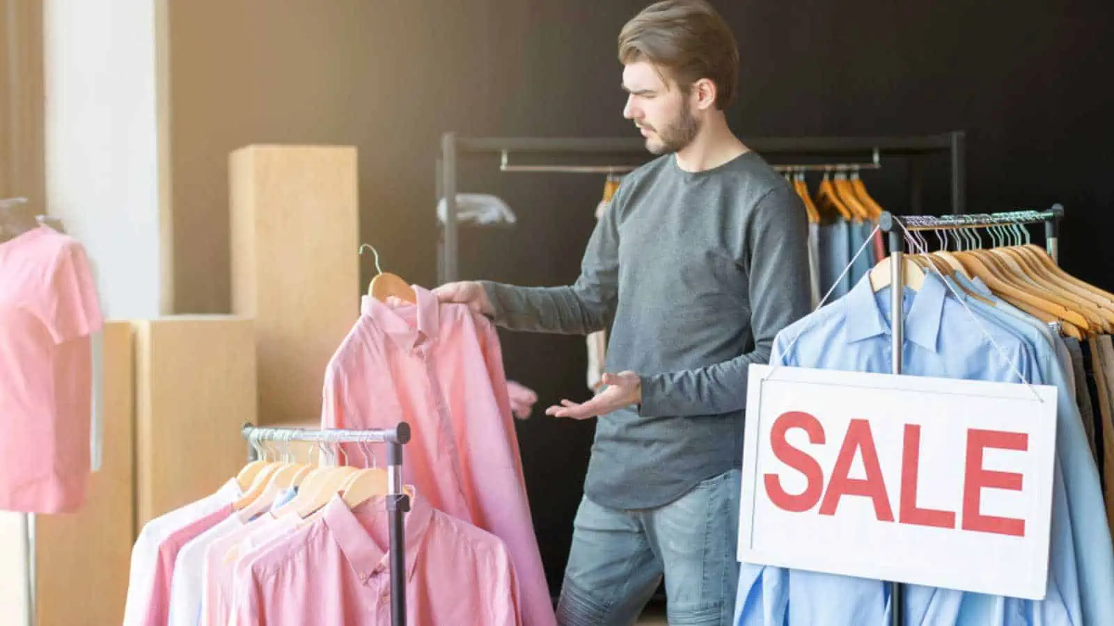 Sales time. Confused caucasian guy choosing shirt at shop, free space