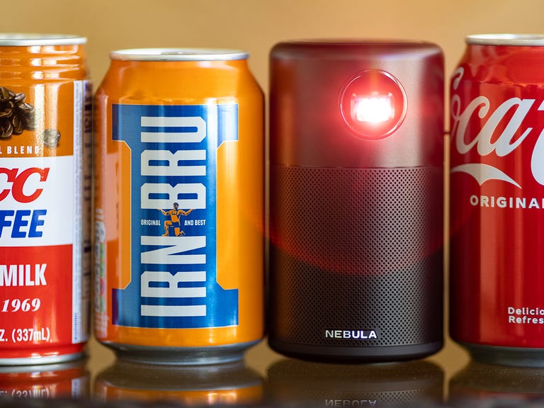 The Anker Nebula Capsule projector beside three soft drink cans