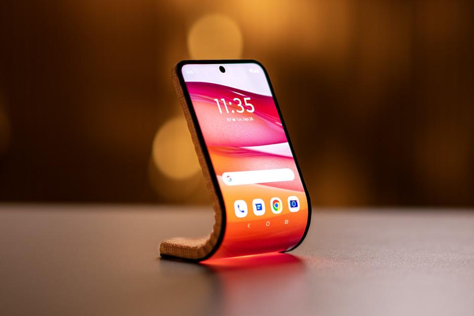 A marketing image from Motorola, showcasing a bendable / rollable phone. The device sits on a table with its bottom serving as a base and its (bent) top protruding upwards like a smart display.