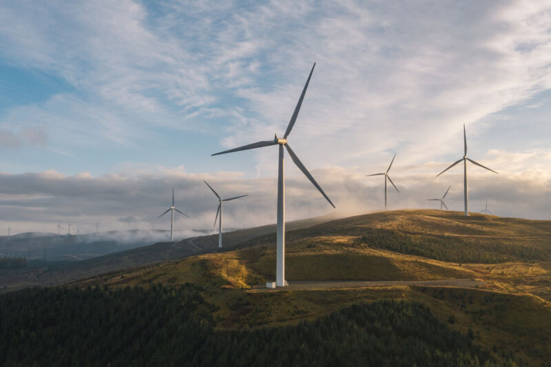 Wind turbines on brown hills against a sunset.