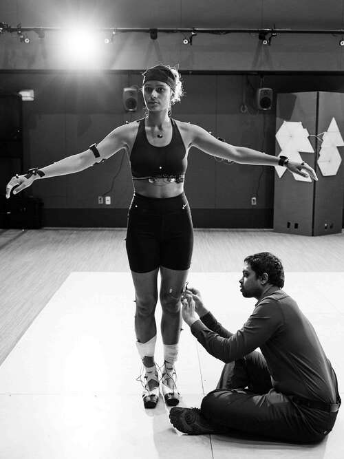 Praneeth sitting on the ground to attach a sensor on the leg of a posed dancer