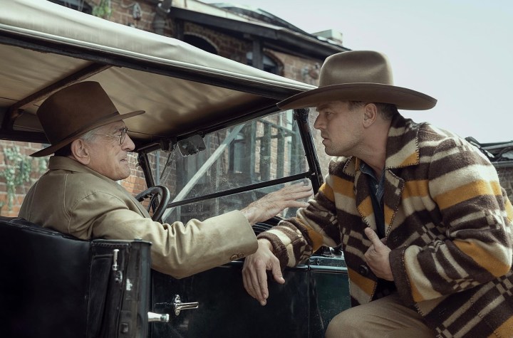 A man leans up against a car while another man holds his arm in Killers of the Flower Moon.