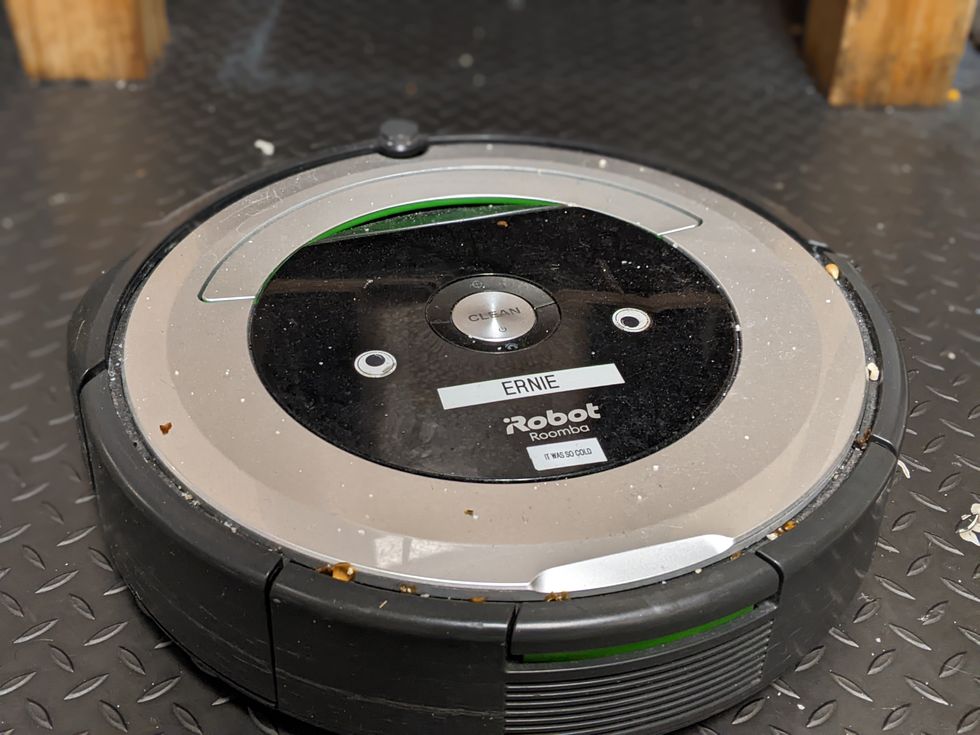 A close up photo of a Roomba on a floor sprinkled with popcorn pieces.