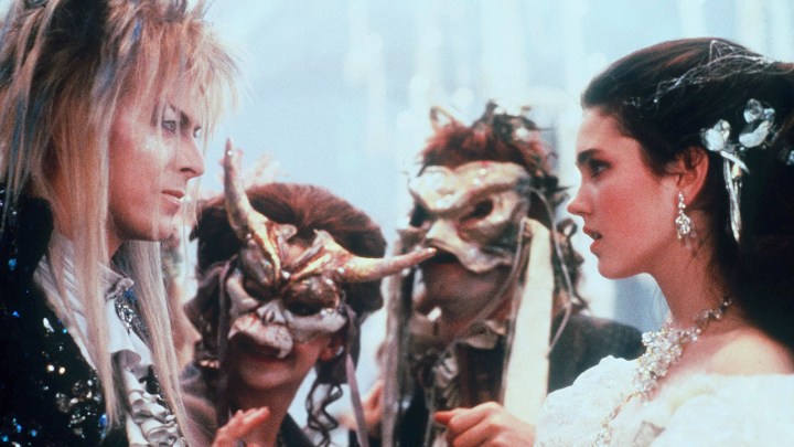 David Bowie and Jennifer Connelly as Jareth and Sarag with two masked characters in Labyrinth.