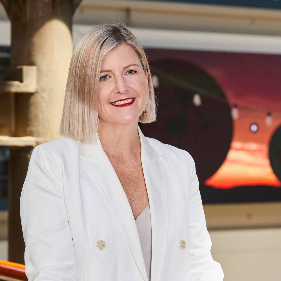 Cicada Innovations chief executive Sally-Ann Williams, wearing a white jacket, smiles at the camera, with a blurry office seen in the background.