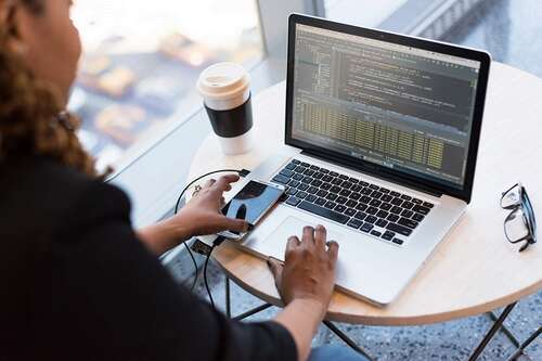 Person working on a Mac while reaching for their phone