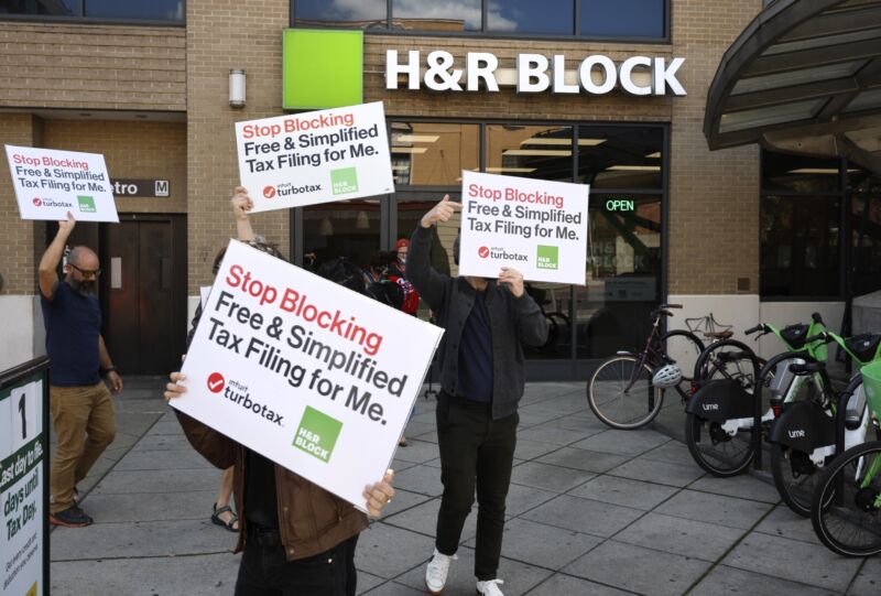 Advocates in front of an H&R Block building hold signs that tell TurboTax and H&R Block to 