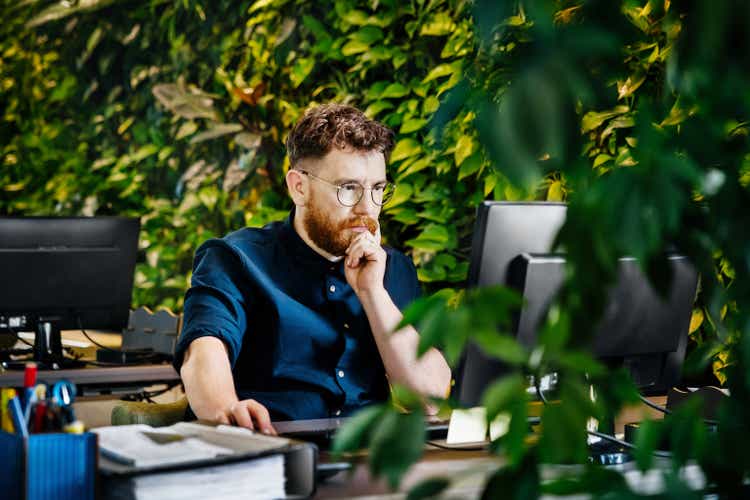 Man Concentrating While Working At Computer Desk In Green Office