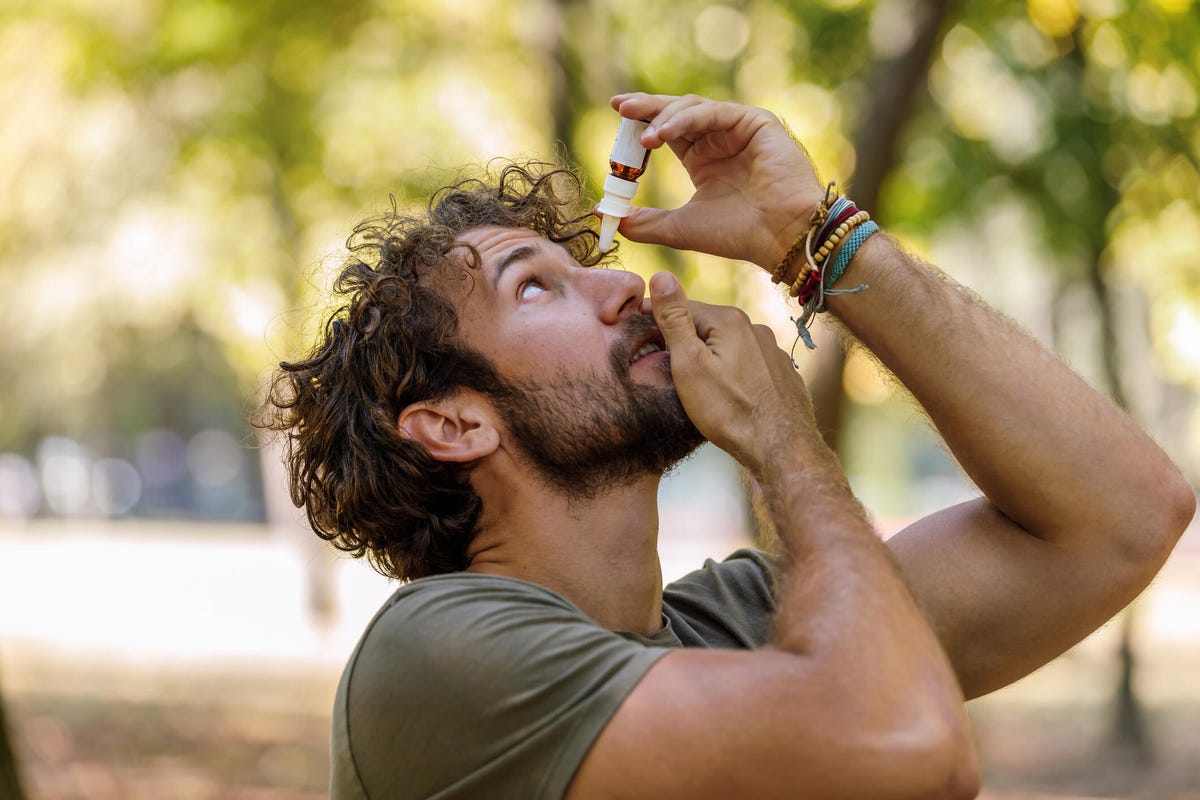 Man putting in eye drops outside.