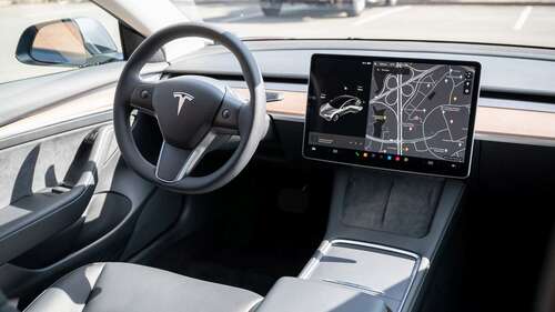 Door handle, steering wheel, infotainment display, wireless chargers, and storage inside the Tesla Model 3