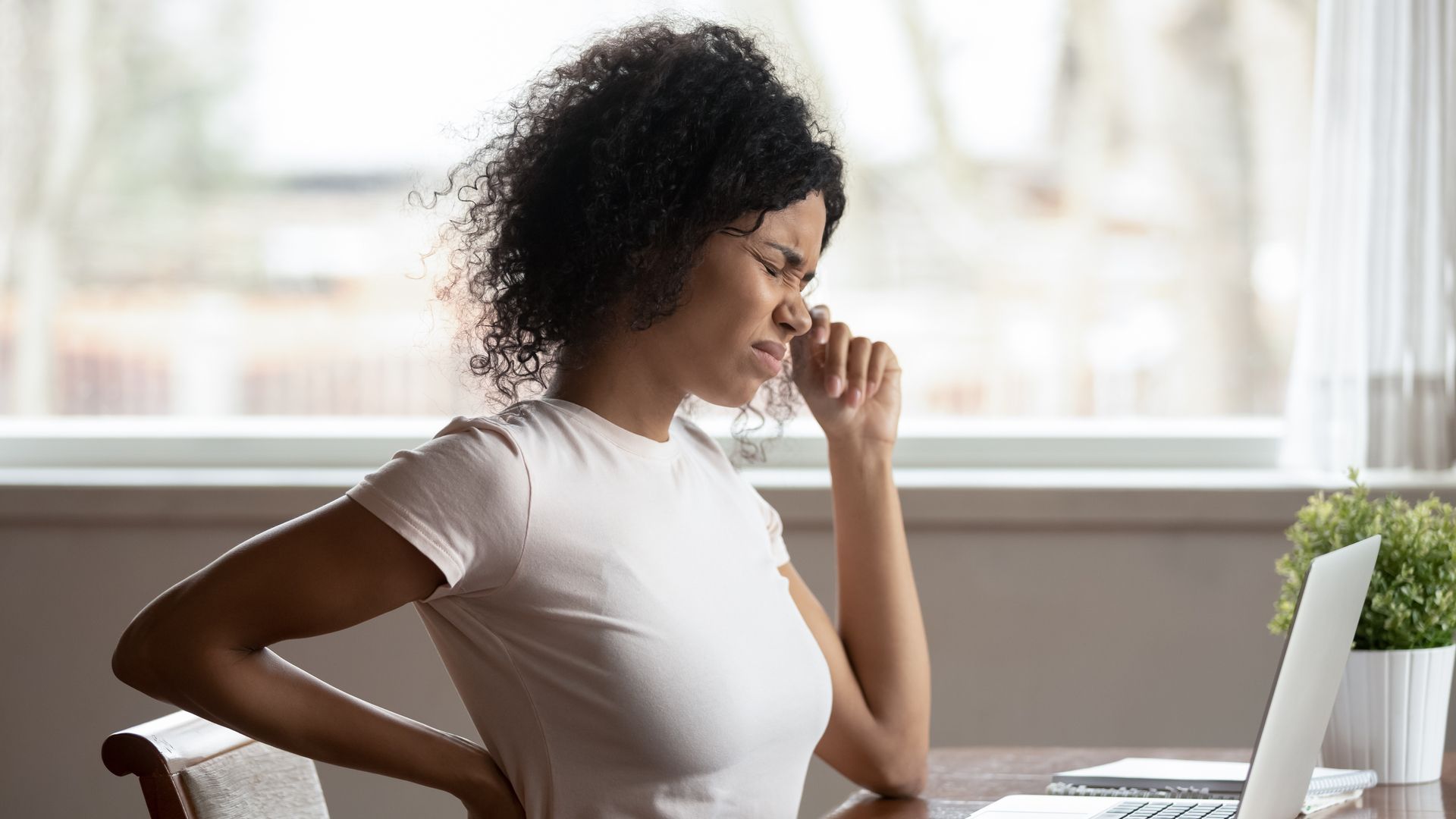 Tired young person sitting at desk touching back suffering from lower back pain.