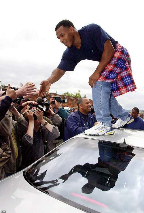 Heavyweight boxer Mike Tyson pictured here wearing a kilt over his jeans and shaking the hands of fans from the top of a different car while on the way to training in Glasgow ahead of the fight in June 2000