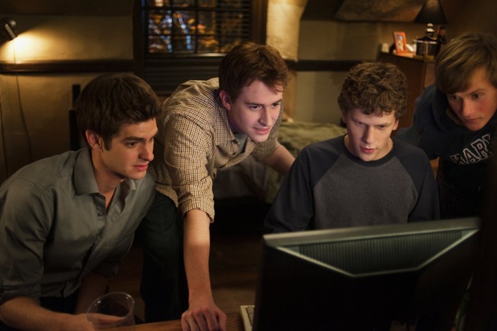 Andrew Garfield and Jesse Eisenberg look at a computer together in The Social Network.