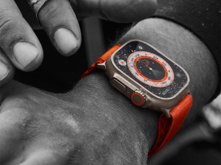 Close up of an orange Apple Watch Ultra on a man's arm.