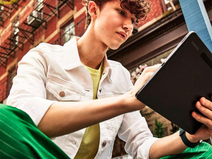 A teenager uses his Samsung Galaxy Tab S8 Ultra on the sidewalk.