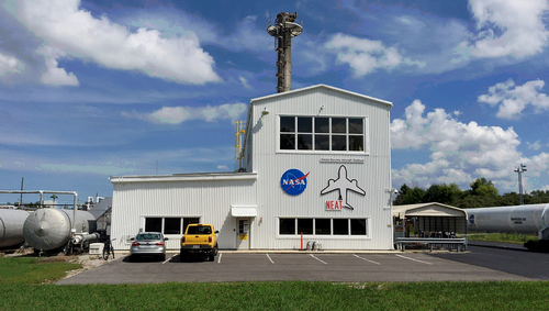 A white, two-story building is surrounded by a small parking lot and large compressed-gas tanks.