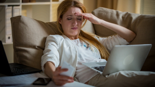 businesswoman on a couch with two cellphones and laptops. Exhausted woman checking her smart phone in office late at night. Responsible executive working, having headache, hands on temples