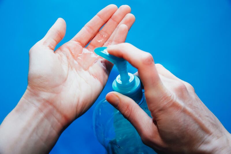 A person holding a bottle of soap and washing their hands.