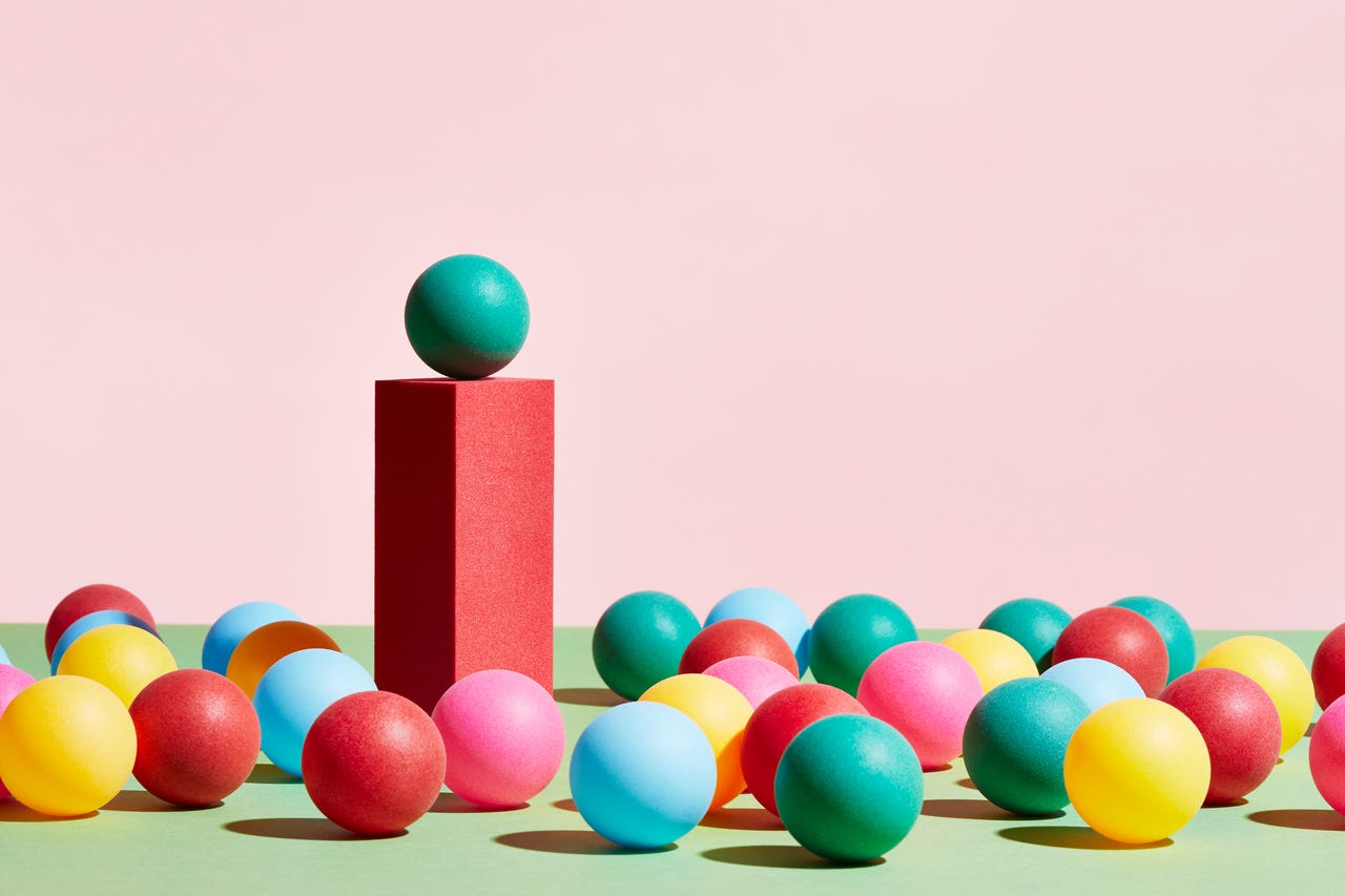 A green sphere stands on top of a pedestal surrounded by a crowd of multicolored spheres