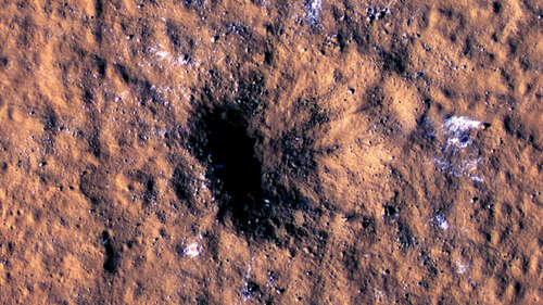 Image of a dark crater on a background of reddish rocks, flecked with snow.