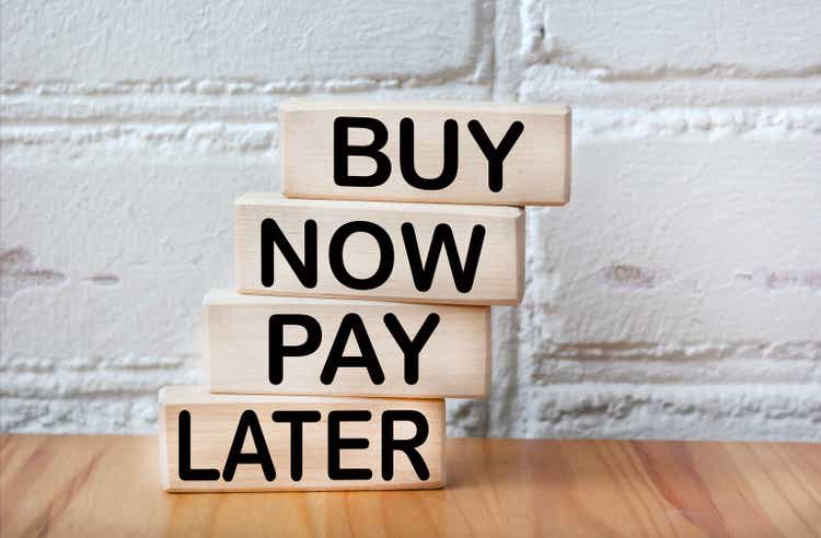 Against the background of a white brick wall, wooden blocks with the text BUY NOW, PAY LATER.