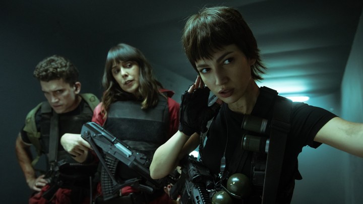 Three people approaching a building stealthily with guns and armor in a scene from Money Heist season 5.