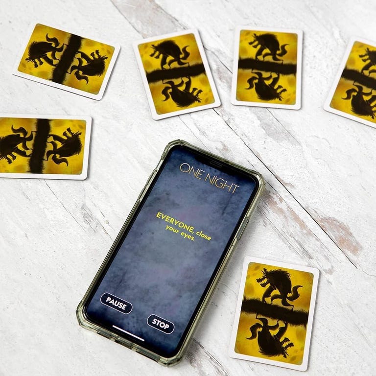 a smartphone displaying the One Night Ultimate Werewolf app while sitting among a number of One Night Ultimate Werewolf cards face down