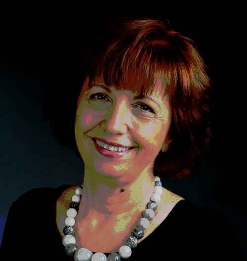 Portrait of a smiling red haired woman in a black shirt and beaded necklace.