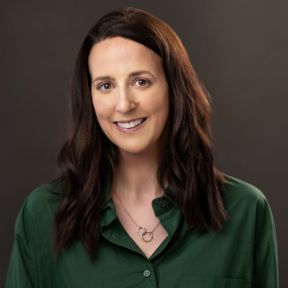 Portrait of a smiling woman with long dark hair and a green button up shirt.