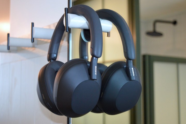 Sony WH-1000XM5 wireless headphones hanging on wall hook in front of a mirror.