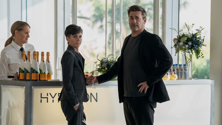 Jon Hamm and Tig Notaro stand in an office lobby in a scene from The Morning Show season 3.