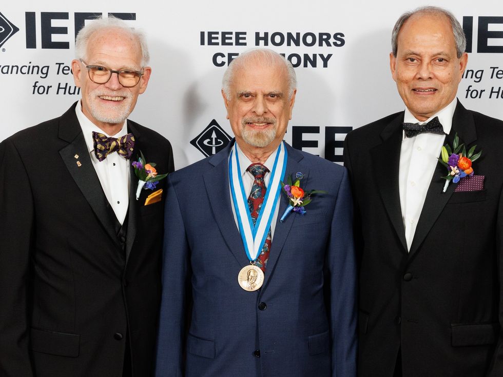 three men standing in suits for a portrait against a white background with black writing