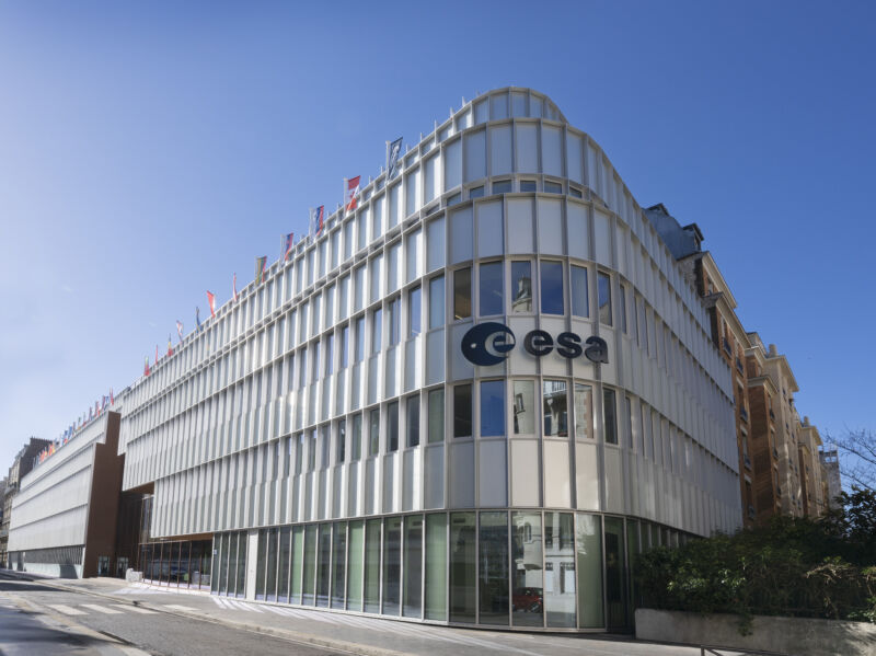 Image of the facade of a building with a curved corner, largely comprised of glass.