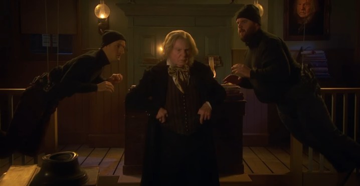 Two men trying to kidnap an actor playing Ebenezer Scrooge in "A Christmas Carol Goes Wrong."