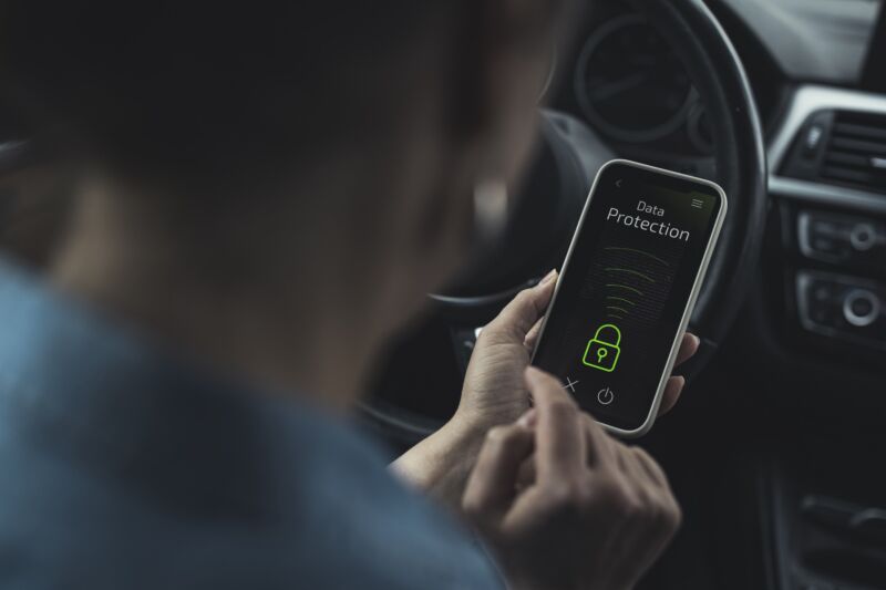 A person sits in a car holding a smartphone, the screen reads 