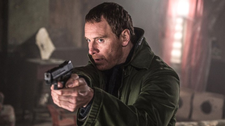 Michael Fassbender as The Killer aiming a gun at something off-camera in The Killer.