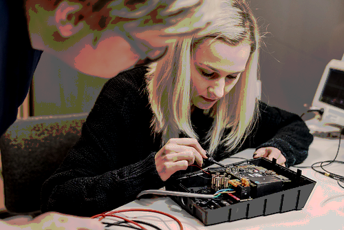 a woman with blond hair working on a device with exposed wires