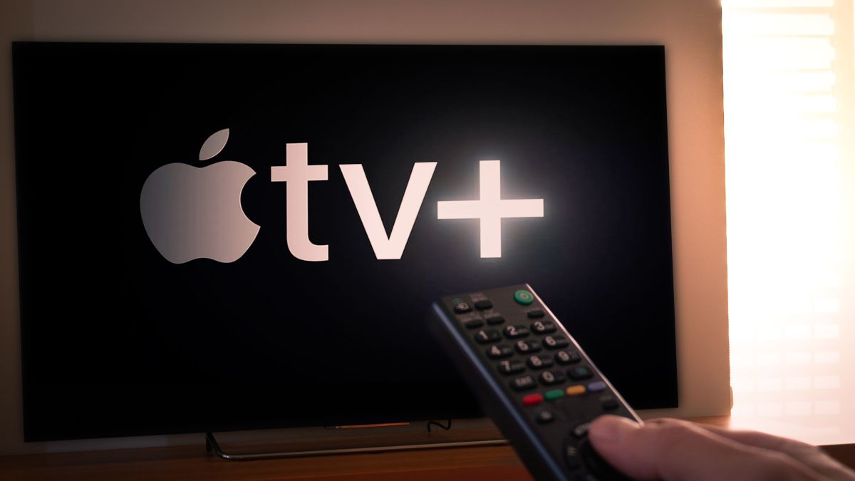 Closeup of a TV remote held in front of a TV with the AppleTV+ logo.