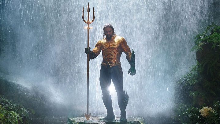 Aquaman standing in front of a waterfall holding a trident in the movie "Aquaman."