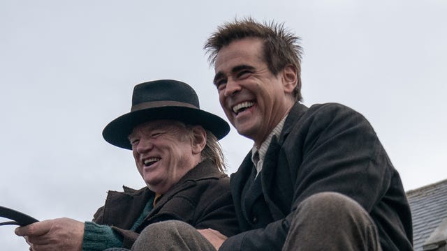 Colin Farrell and Brendan Gleeson laugh while riding a wagon in the movie The Banshees of Inisherin.