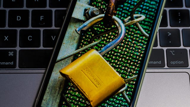 Unlocked padlock and fencing on a phone screen, with a computer keyboard in the background