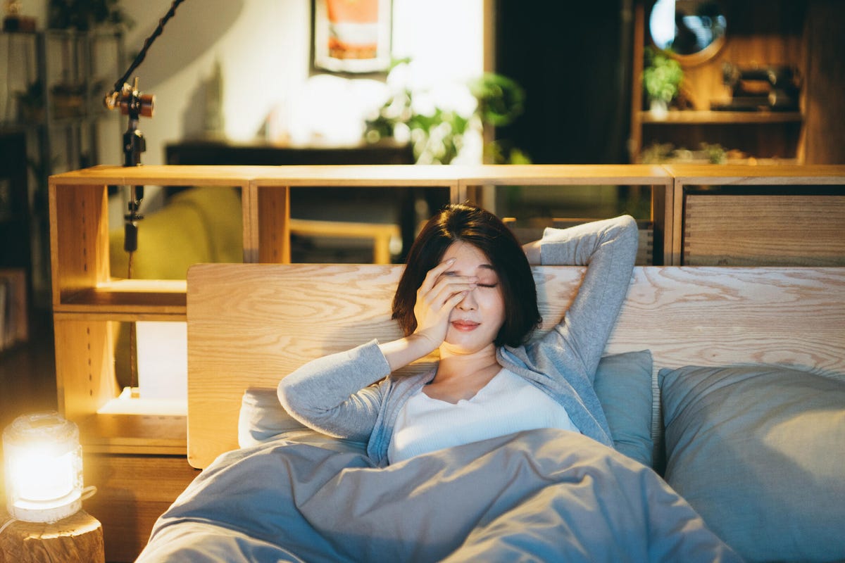 A young woman laying in bed rubbing one eye