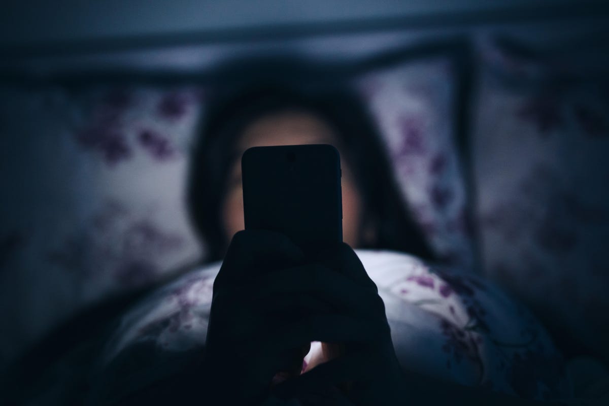 A person holding a phone up to her face, glowing in the dark