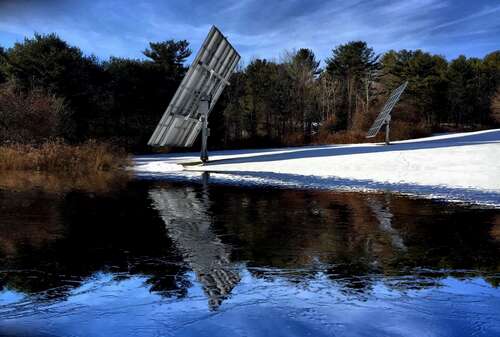 Solar panels and their reflection on a barely frozen lake.