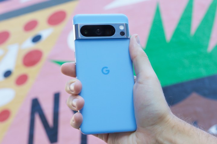 Someone holding the Google Pixel 8 Pro in front of a colorful background.