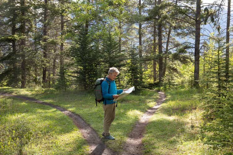 Hiker stops at forked forested trail and looks to map for direction