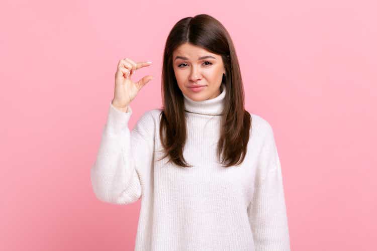 Young adult woman showing a little bit gesture, inch or centimeter, disappointed with minimum size.