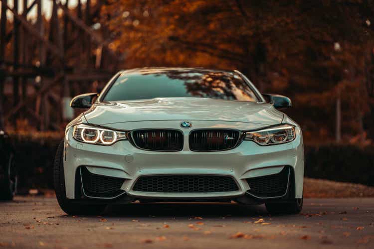 Front of a white BMW M4 parked on a street with trees in the background