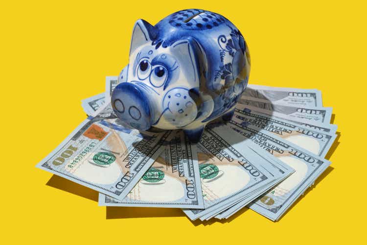 ceramic piggy bank standing on dollars. America dollars banknotes money into piggy bank on yellow background. Piggy Bank. close up of dollar cash money and piggy bank on table.