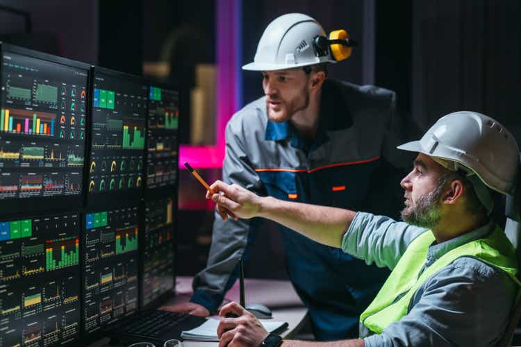 Head engineer and worker following factory production line uses screens with Industry 4.0 software. Couple of facility operators checking and analysing process